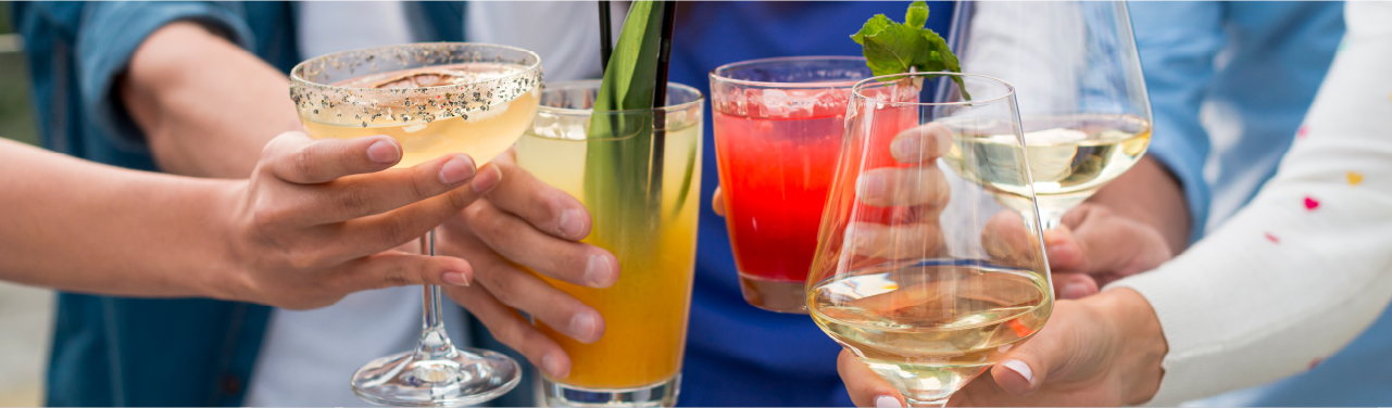 A group of people raising a variety of colorful cocktails and wine glasses, celebrating together in a casual outdoor setting.