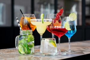 A variety of colorful cocktails displayed in different glasses, garnished with fruit and mint.