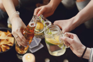 A group of friends toasting with mason jar cocktails and beer bottles, surrounded by snacks and playing cards, creating a fun and casual party atmosphere.