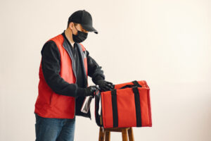 A delivery man wearing a mask and gloves sanitizing a red delivery bag, demonstrating safe and hygienic handling practices.