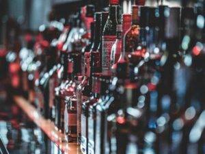 A variety of alcohol bottles lined up on a shelf, featuring a range of liquor brands with blurred backgrounds, creating a bokeh effect