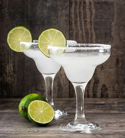 Two margarita cocktails with salted rims and lime garnishes on a wooden surface.