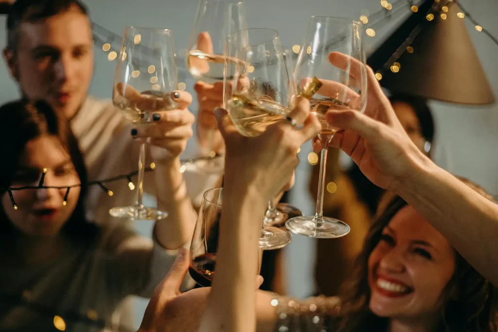 Group of friends raising wine glasses in celebration with festive lights in the background, highlighting the ease of booze delivery near me in Brampton and the GTA.