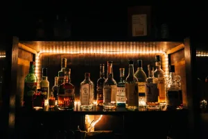 A collection of liquor bottles on a backlit wooden shelf, showcasing whiskey, gin, and other spirits.