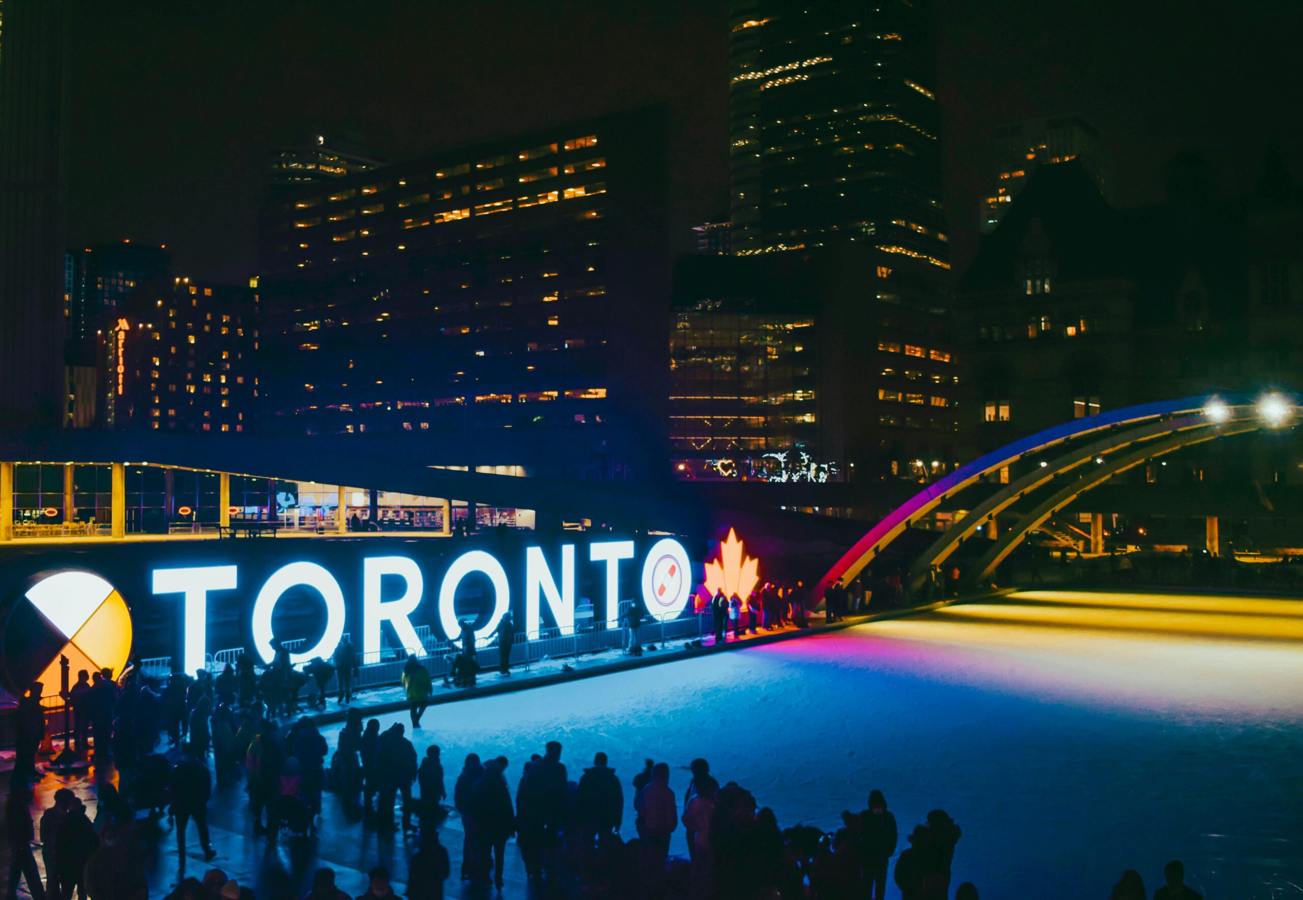 Illuminated Toronto sign with people skating on an ice rink at night.