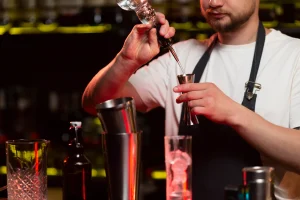 Male bartender preparing a cocktail using a shaker and measuring tool at a bar